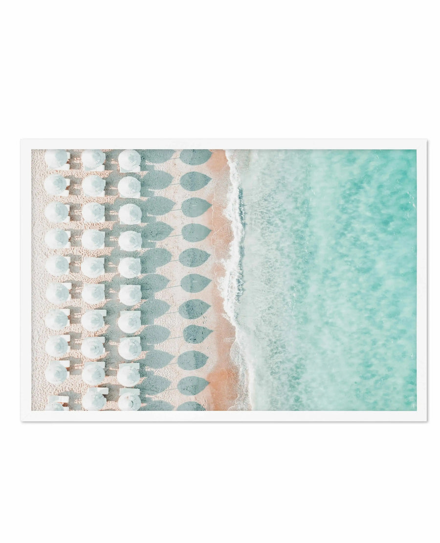 Aerial view art print showing rows of white beach umbrellas casting gray shadows on pale sand, adjacent to turquoise shallow water with visible ripples and foam. Watercolor or digital painting style with soft, muted tones of cream, sage green, and aqua. White border framing. Composition emphasizes geometric patterns of umbrellas contrasting with organic water textures.
