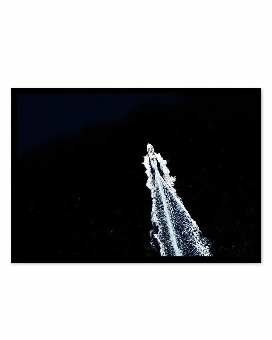 "Aerial photograph art print of a white speedboat creating a long, frothy wake as it cuts through dark, still water, printed on fine art paper with a matte finish."