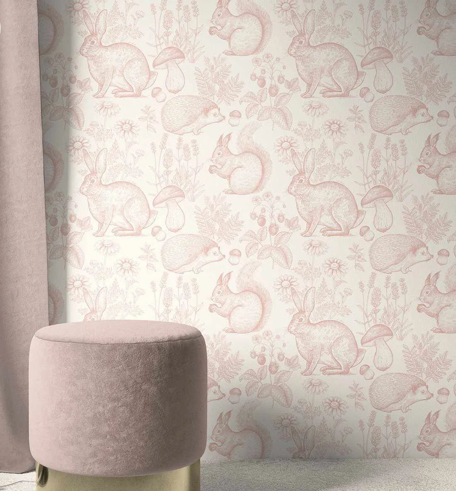 Peel and stick wallpaper featuring a repeating pattern of woodland animals and flora in a delicate dusty rose pink on a soft cream background. The design includes detailed illustrations of rabbits, hedgehogs, and squirrels, interspersed with mushrooms, wildflowers, and berry bushes, giving it a whimsical, hand-drawn quality. A plush, round, dusty rose pink velvet ottoman with a gold base is visible in the foreground, and a matching dusty rose curtain hangs on the left.