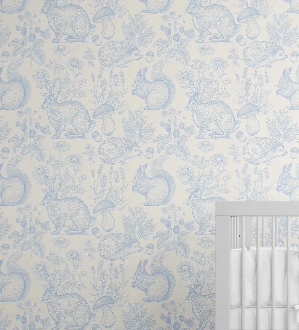 Woodland Folk Wallpaper in Sky Blue featuring a repeating pattern of forest animals and botanicals rendered in soft blue line drawings on a cream background. The design includes rabbits, squirrels, hedgehogs, and mushrooms interspersed with delicate wildflowers, ferns, and botanical elements. The illustration style appears hand-drawn with fine linear detailing. A white painted crib is visible in the lower right corner, showing how the wallpaper coordinates with nursery furnishings.