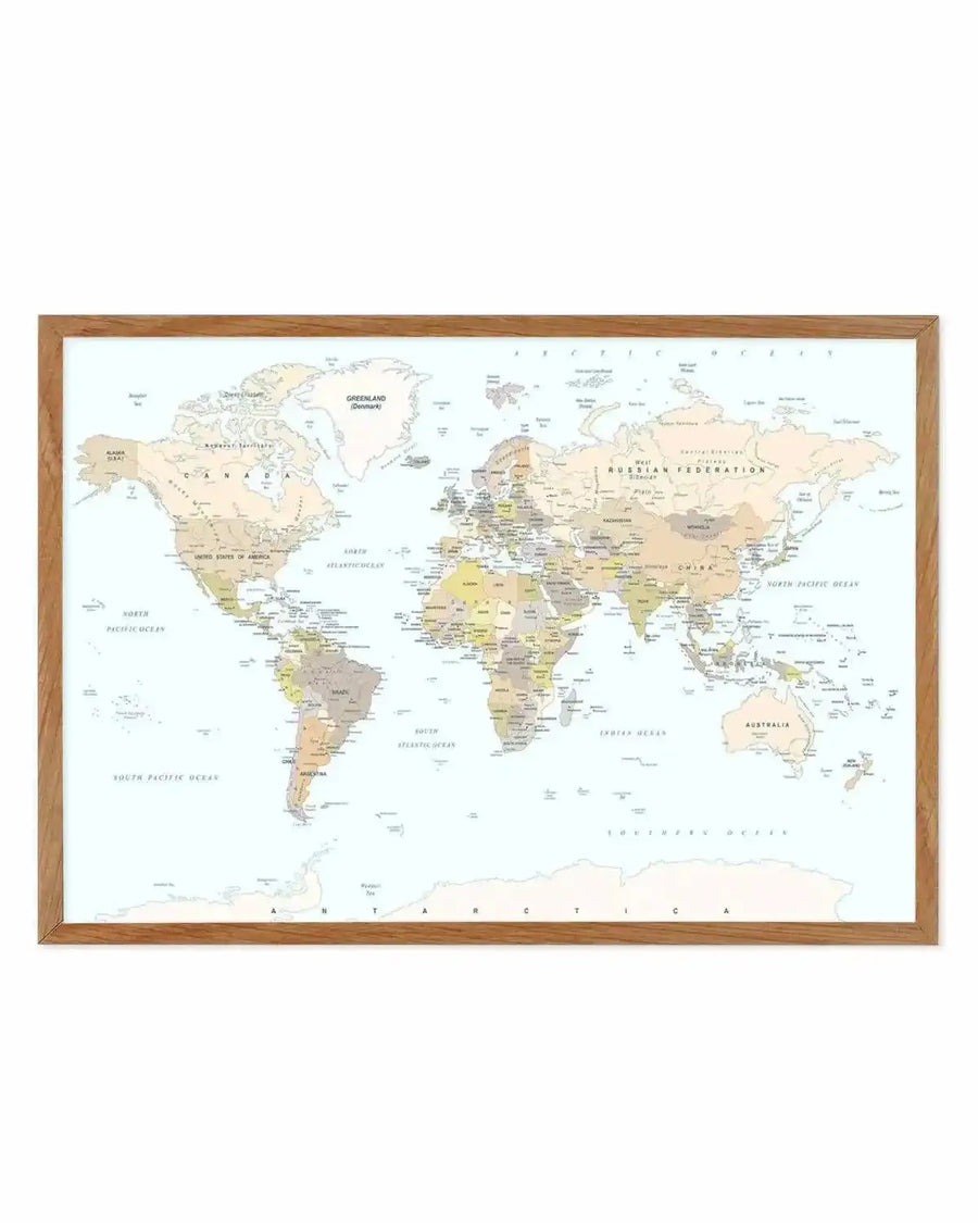 Framed world map art print with wooden tan frame displaying all continents and countries in soft muted tones of cream, pale yellow, tan, and grey with blue oceans. Country borders and city labels are printed in small dark text. The map shows Antarctica at the bottom and includes inset boxes for Greenland and Australia. White border surrounds the map within the frame.