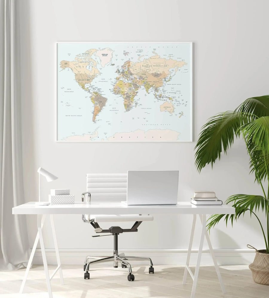 Classic world map art print in natural oak frame, hung above white desk with laptop and green plant