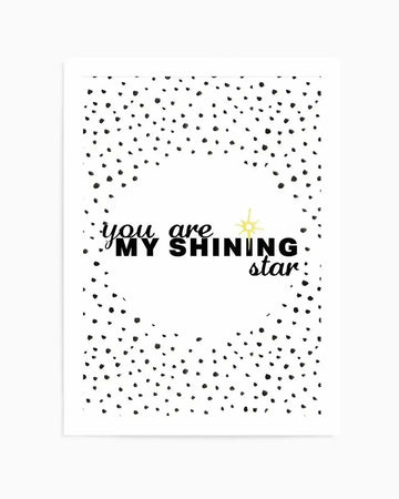 Art print featuring black hand-drawn text reading "you are MY SHINING star" in mixed typefaces, with a small yellow illustrated star above the word "SHINING." The background is white with a scattered pattern of small black dots and dashes forming a loose border around the central text, creating a night sky effect. The overall composition has a minimalist, encouraging aesthetic with a combination of bold and cursive lettering styles.