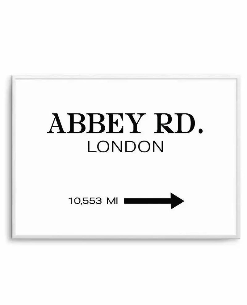 Framed art print with a white background and black text. The text reads "ABBEY RD." in large, bold serif font, followed by "LONDON" in a smaller, sans-serif font below it. In the bottom left corner, the text "10,553 MI" is displayed, with a black arrow pointing to the right next to it. The print is displayed in a white frame.