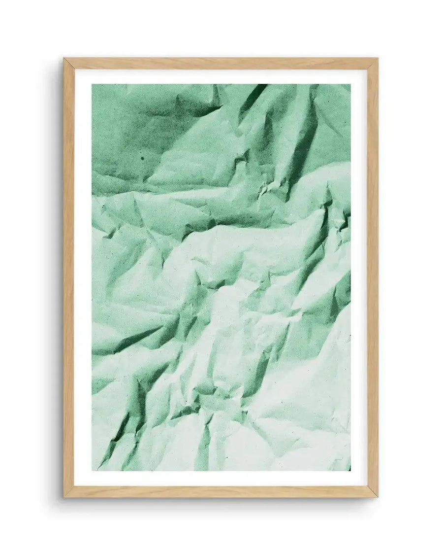 Abstract art print featuring a crumpled paper texture in varying shades of mint green and pale sage, with deep shadows creating a three-dimensional effect, displayed in a natural oak frame with white border.