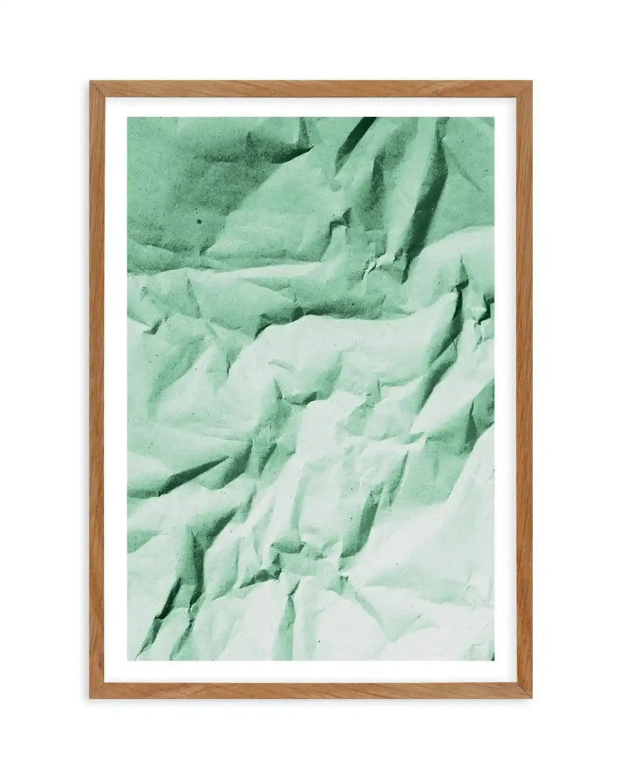 Abstract art print featuring a crumpled paper texture in varying shades of light to medium mint green, creating deep shadows and highlights across the surface, displayed in a natural oak frame with white border.