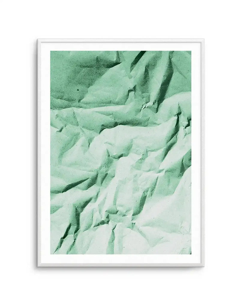 Abstract art print featuring a crumpled paper texture in varying shades of muted sage green, from darker tones at the top to lighter, almost mint green at the bottom. The composition highlights the deep creases and folds of the paper, creating a dynamic interplay of light and shadow, displayed in a white frame with a white border.