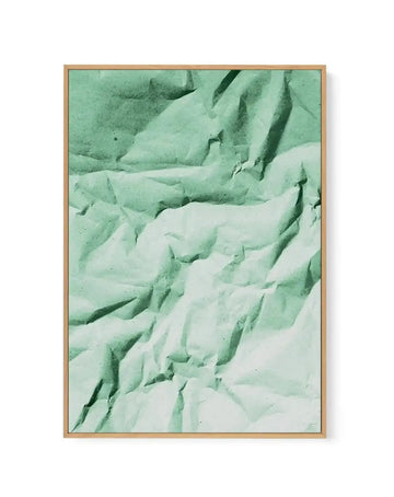 Framed canvas art print featuring an abstract composition of layered, undulating forms in soft sage green, mint green, and cream tones. The textured surface creates depth through diagonal striations and shadowed ridges that resemble folded fabric or geological formations. The image has a muted, monochromatic quality with subtle variations in tone and shadow. The canvas is mounted in a natural wood frame with a clean, simple border.