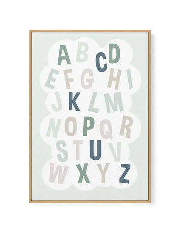 Framed canvas art print featuring the complete alphabet arranged in rows within soft, overlapping cloud shapes. Letters in varying shades of sage green, dusty blue, soft gray, and cream create a gentle color palette. The background is a pale sage green. Natural wood frame with white border surrounding the design. Suitable for nursery or child's room decor.