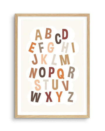 Art print featuring the alphabet in a playful, scattered arrangement of uppercase letters, each in a different earthy tone such as terracotta, rust, beige, brown, and cream, against a soft cream background with subtle white cloud shapes. The print is displayed in a natural oak frame with a white border.