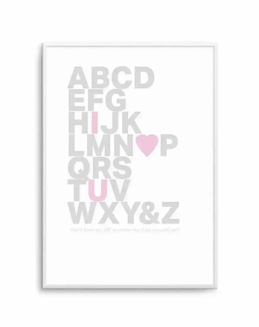 Framed art print featuring the complete alphabet arranged vertically in large, light gray capital letters. A pink heart replaces the letter O, and the letters I, U, and V are highlighted in soft pink. The design is set against a white background within a white frame with a white border. Small text appears at the bottom of the print. The overall aesthetic is minimalist and modern.