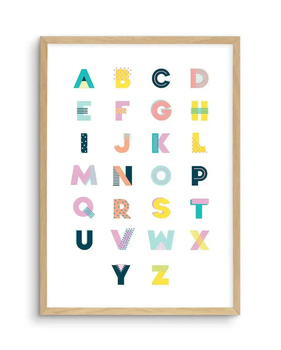 "Alphabet art print featuring uppercase letters A-Z in a grid, each letter with a unique geometric pattern and bright, contrasting colours like teal, yellow, pink, and blue, printed on fine art paper and displayed in a natural oak frame with white border"