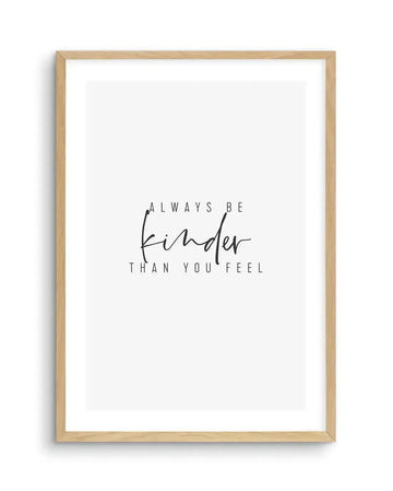 Art print featuring the phrase "ALWAYS BE kinder THAN YOU FEEL" in black text on a white background, with "kinder" in a flowing script font and the rest in a simple sans-serif font, displayed in a natural oak frame with white border.