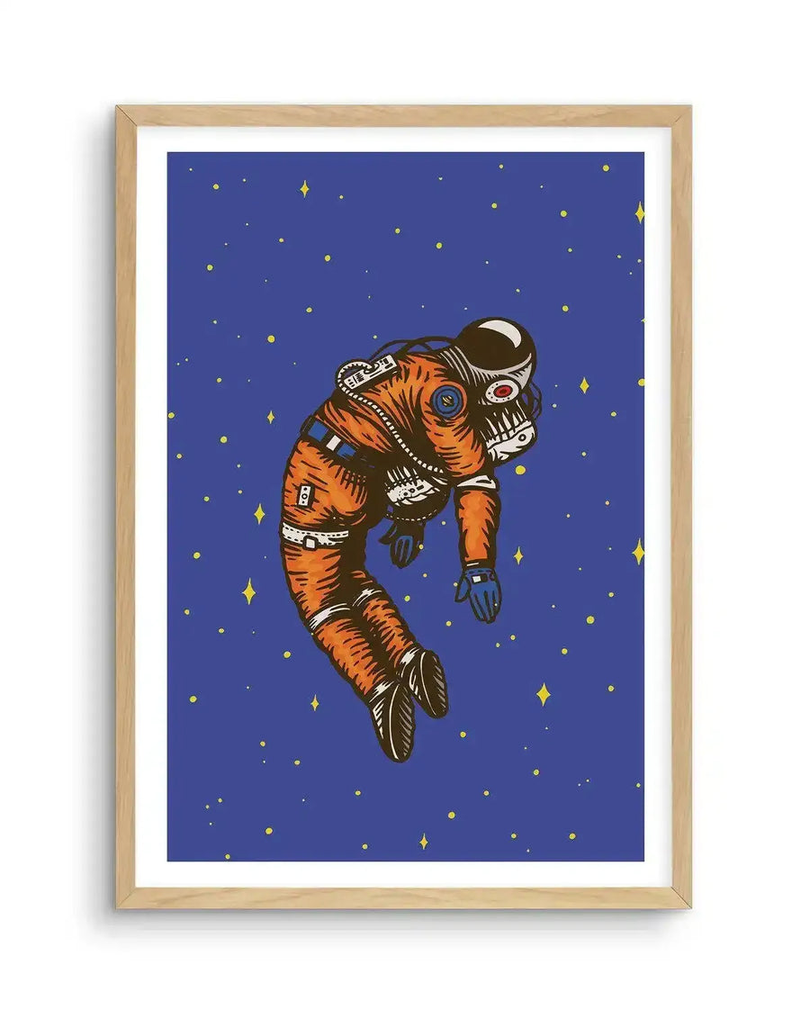 Art print featuring an illustration of an astronaut floating in outer space against a deep blue background with scattered yellow stars. The astronaut wears an orange suit with visible details like straps and buckles, and a dark helmet with a red visor, depicted in a slightly slumped, relaxed posture. The print is displayed in a natural oak frame with a white border.