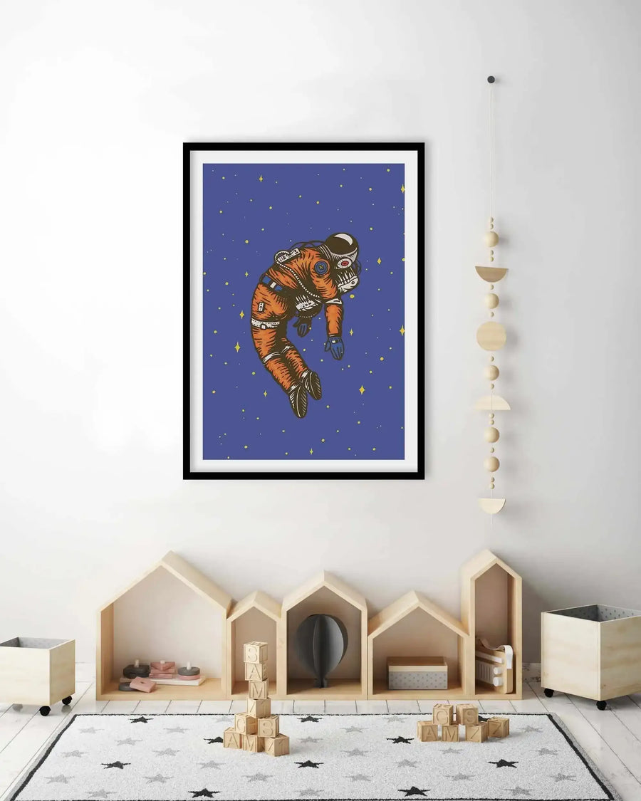 Kids Room:
Large framed art print displayed above a row of house-shaped wooden shelves in a child's room. The print features an astronaut in an orange and brown spacesuit floating against a dark blue background with scattered yellow stars, with a black frame and white border. A wooden moon phase mobile hangs to the right of the print, and a white rug with black and grey stars covers the floor.