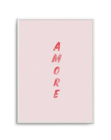 Framed art print on light pink background with the word "AMORE" written vertically in red hand-drawn lettering with a sketched, marker-like texture. The print is displayed in a silver-gray frame with white border. The composition is centered on a soft, pale pink background with ample negative space around the red text.