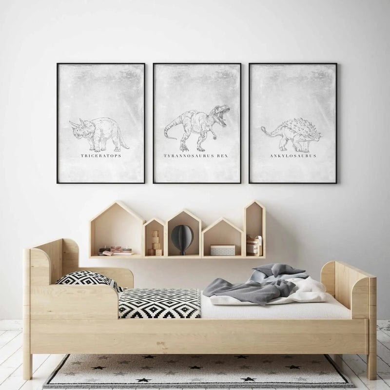 Framed pencil sketch illustration of Ankylosaurus dinosaur labeled with scientific name, displayed on white wall above wooden child's bed with natural wood frame and house-shaped shelving unit, shown as part of three-print dinosaur series with black frames and white borders.