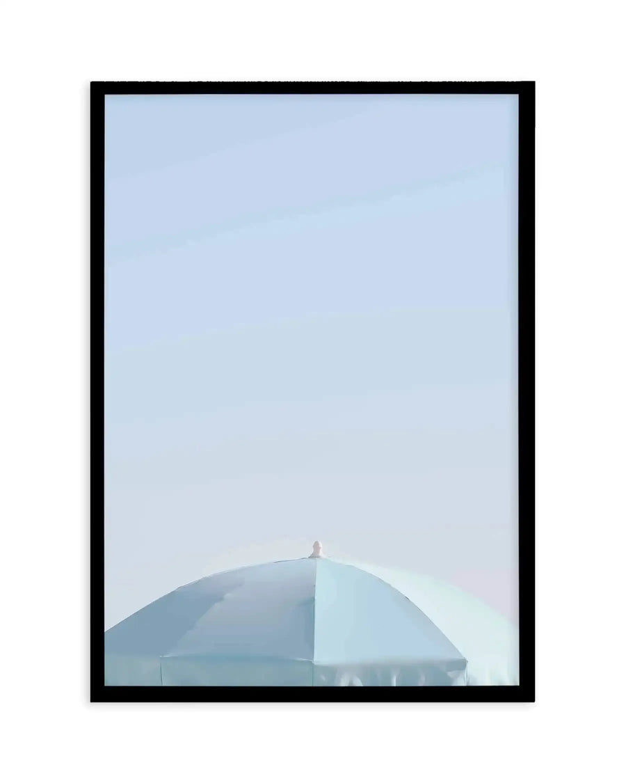 Framed photograph of the top of an aqua blue parasol against a clear, pale blue sky, with a black frame and white border. The parasol is seen from a low angle, filling the bottom third of the frame, with its peak pointing upwards. The sky is a soft, uniform light blue, suggesting a bright, sunny day.