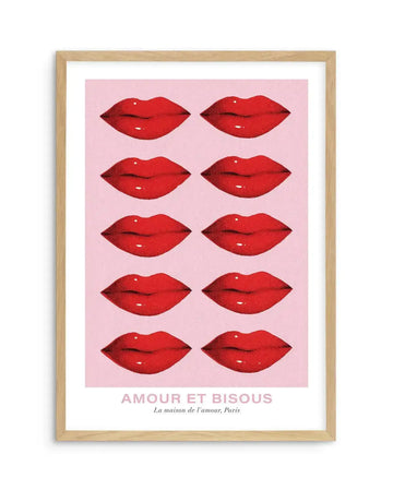 Art print featuring ten pairs of glossy red lips arranged in five rows of two on a pale pink background, with the text "AMOUR ET BISOUS" and "La maison de l'amour, Paris" at the bottom, displayed in a natural oak frame with white border.