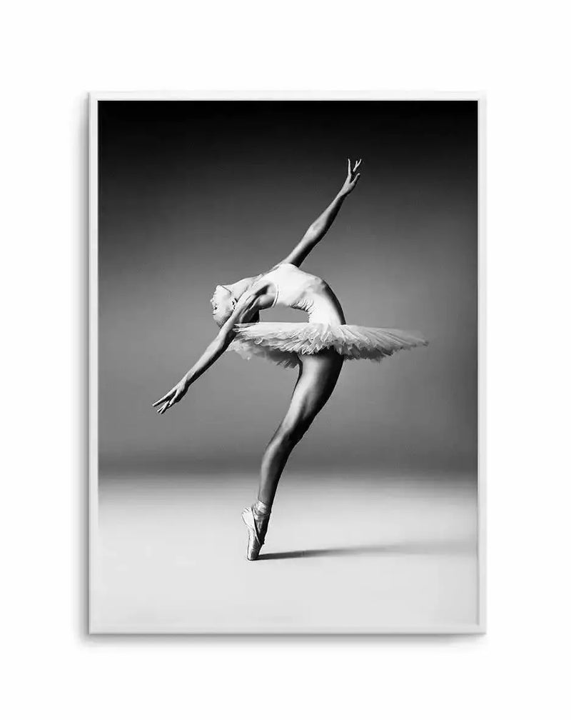 Framed black and white photograph of a ballerina in a classical pose, captured mid-dance with her body arched backward and arms extended. She is wearing a white tutu and pointe shoes, with her head tilted back and eyes closed, conveying grace and emotion. The background is a soft gradient from dark grey at the top to light grey at the bottom, creating a dramatic contrast.