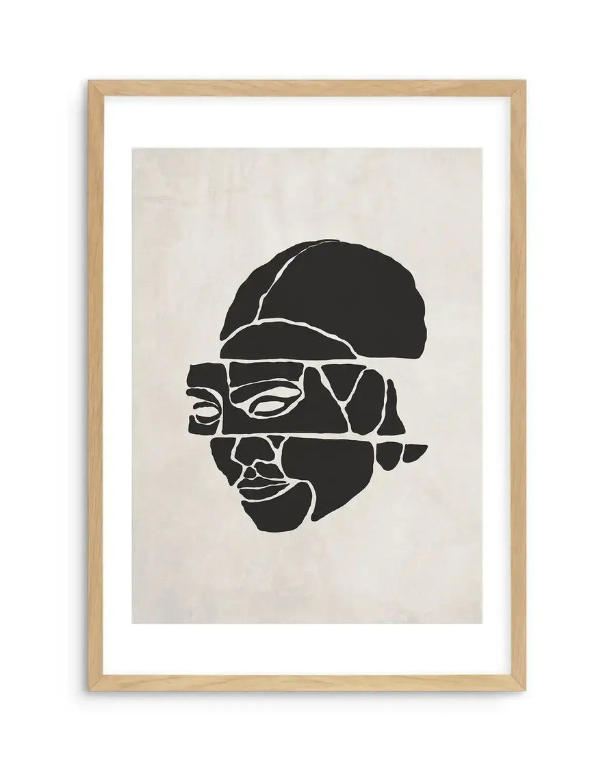 Abstract art print featuring a fragmented face in solid black against a warm cream background, printed on fine art paper and displayed in a natural oak frame with white border. The face is composed of disconnected geometric shapes, with the top of the head and the lower face separated by a horizontal gap.