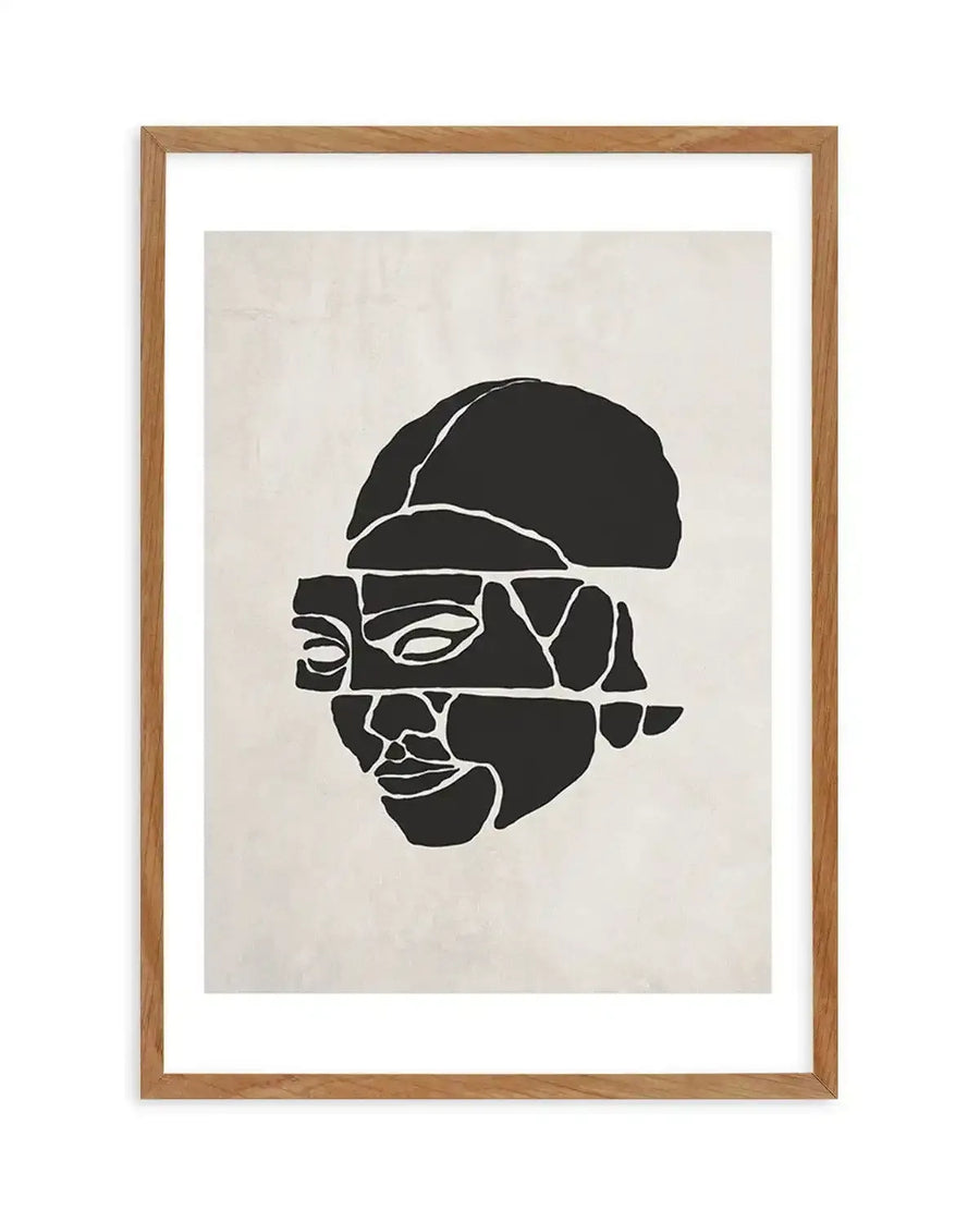 Abstract art print featuring a fragmented face in solid black against a warm off-white background, printed on fine art paper and displayed in a natural oak frame with white border. The face is composed of irregular geometric shapes, with visible eyes, nose, and mouth, and a rounded shape suggesting the top of the head.