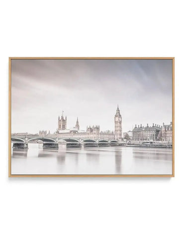 Framed canvas print of a long-exposure photograph of the Houses of Parliament and Big Ben in London, rendered in a muted, almost monochromatic palette of soft greys and whites. The iconic buildings and Westminster Bridge are reflected in the smooth, still surface of the River Thames, with a hazy, overcast sky above. The print is displayed in a natural oak frame.