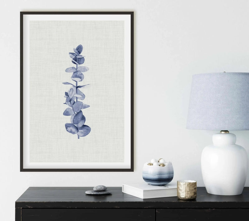 Watercolour art print featuring a single eucalyptus branch with blue-grey leaves and visible brushstroke texture on a textured cream background, printed on fine art paper and displayed in a black frame with white border
