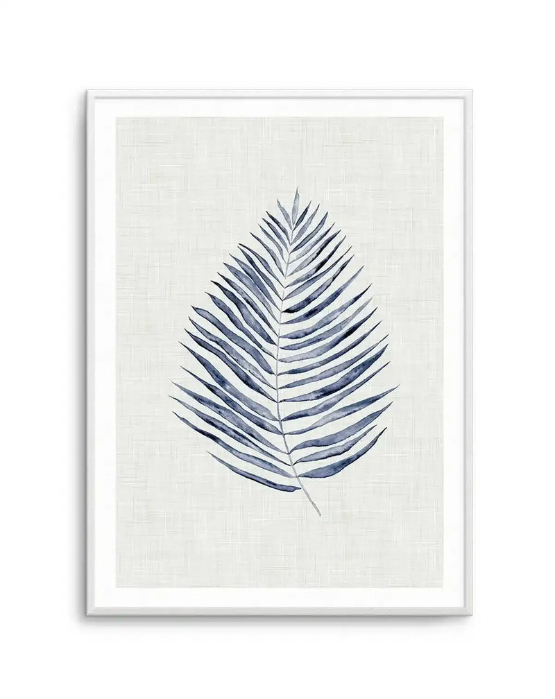 Watercolour art print featuring a single palm frond in shades of indigo and slate blue, with visible brushstroke texture, on a cream background with a subtle woven texture, displayed in a white frame with a white border.