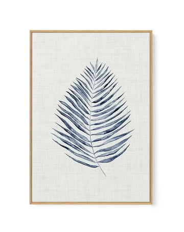 Framed canvas art print featuring a single blue-grey fern leaf rendered in watercolor against a cream textured background. The fern displays symmetrical leaflets arranged along a central stem, with darker navy shading on the left side of each leaflet creating dimensional depth. The artwork is centered on the canvas within a natural wood frame with a white border.