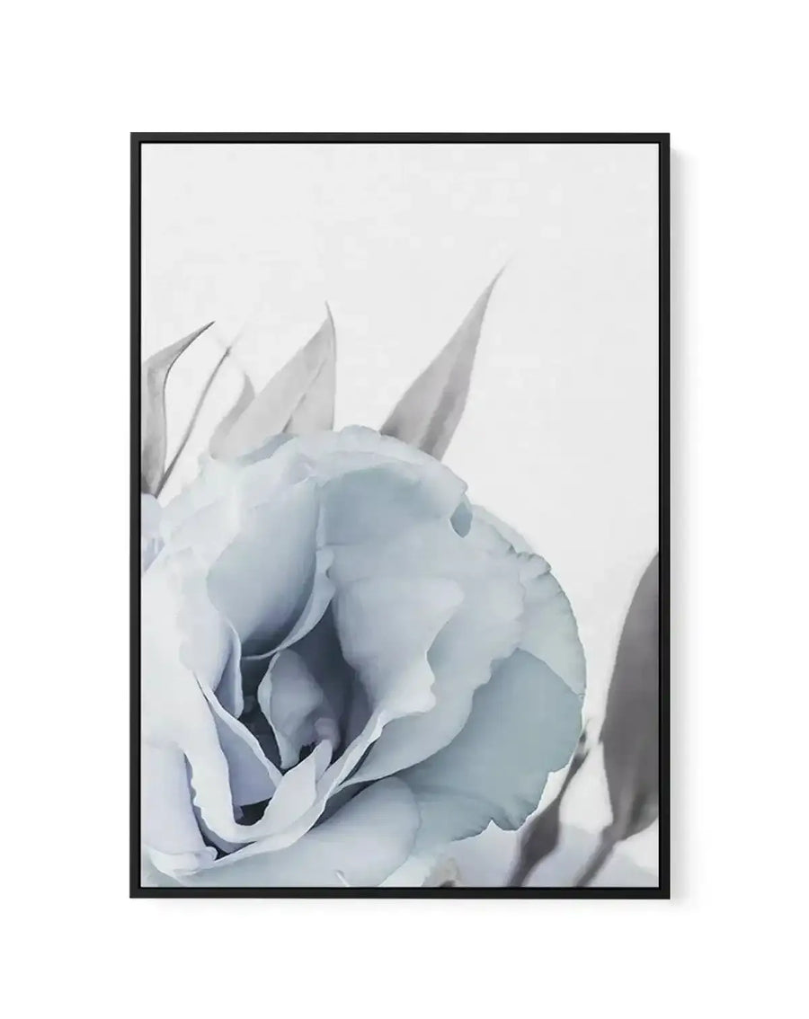 Framed canvas art print featuring a close-up of a blue lisianthus flower with pale blue and white petals in soft focus. The flower displays layered, ruffled petals with delicate pointed sepals extending upward against a light gray background. The composition emphasizes the flower's dimensional texture and subtle color gradations. The artwork is enclosed in a black frame with a white border.