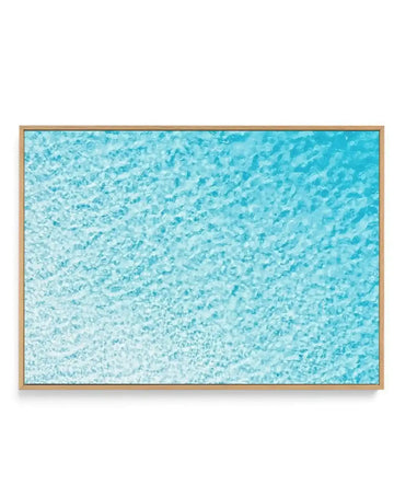 Canvas print of an aerial photograph of clear turquoise ocean water with ripples and reflections creating a textured surface, displayed in a natural wood frame.
