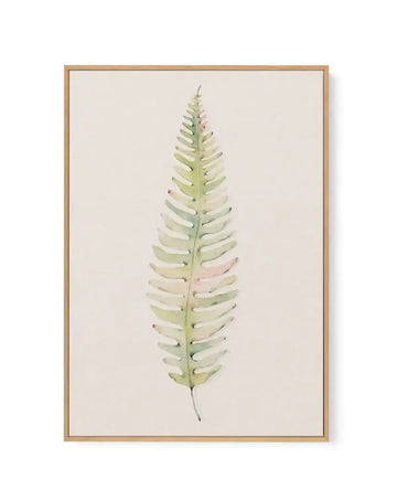 Watercolor painting of a single fern frond displayed in a natural wood frame with white border. The fern features delicate, symmetrical leaflets in soft green, sage, cream, and pale blush pink tones, arranged along a slender central stem. The composition is centered vertically on a light beige background. The artwork has a gentle, botanical illustration style with subtle color variations and a naturalistic aesthetic.