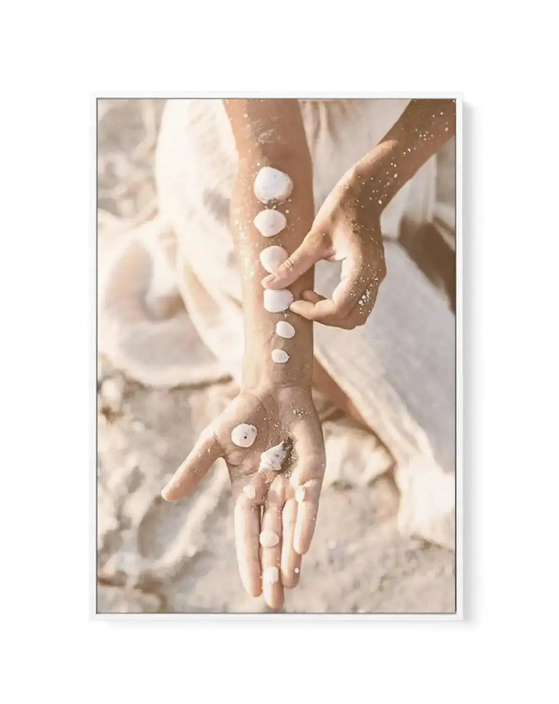 Framed canvas art print depicting two people's arms and hands adorned with white circular dots applied like body art, set against a warm, sandy beach background. The composition shows intertwined arms in soft beige and tan tones with golden glitter accents across the skin. The artwork has a bohemian, artistic aesthetic with a dreamy, sun-bleached color palette of cream, ivory, and warm bronze. The canvas is displayed in a light gray frame with a white border.