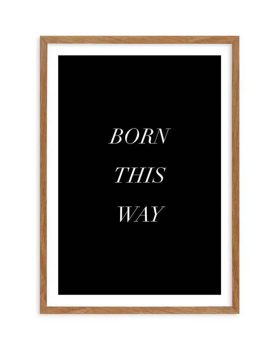 Art print featuring the words "BORN THIS WAY" in three lines of elegant, serif, italicized white text on a solid black background, displayed in a natural oak frame with white border.