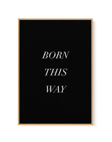 Framed canvas art print with natural wood frame displaying the phrase "BORN THIS WAY" in white italic serif typography centered on a solid black background. The canvas has a matte finish with clean, minimalist design and is shown mounted on a white wall.