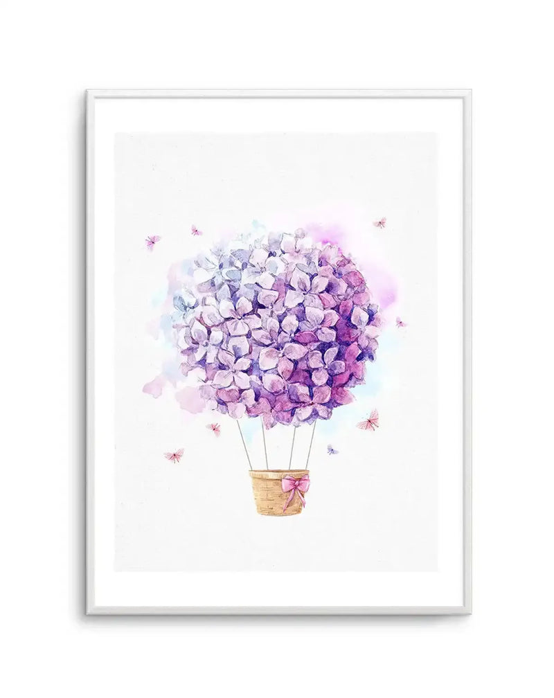 Watercolor art print featuring a hot air balloon made of purple and lavender hydrangea flowers with a woven basket suspended below by thin stems. Soft watercolor washes in purple, pink, and blue tones surround the balloon. Tiny pink and purple flowers float around the composition. Displayed in a silver-toned frame with white border against a light background.