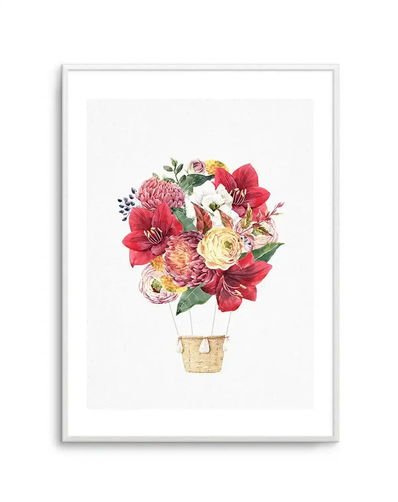 Watercolour art print featuring a hot air balloon composed entirely of a vibrant bouquet of flowers against a white background, printed on fine art paper and displayed in a white frame with white border. The bouquet includes large red amaryllis, pink protea, yellow ranunculus, white anemones, and small blue berries, with green leaves interspersed. A small woven basket with white tassels hangs below the floral balloon.