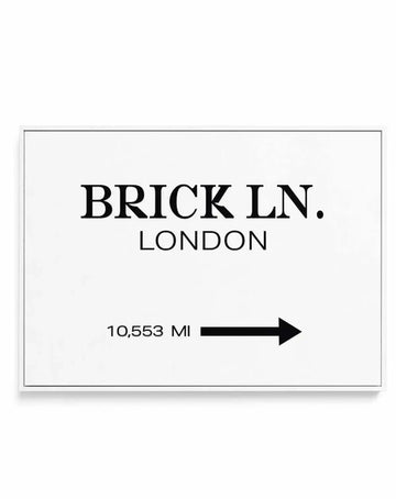 Framed canvas art print displaying "BRICK LN. LONDON" in bold black serif lettering centered on a white background, with "10,553 MI" and a rightward-pointing black arrow below. Simple black border frame with white border surrounding the design. Clean, minimalist typography in a horizontal rectangular format.
