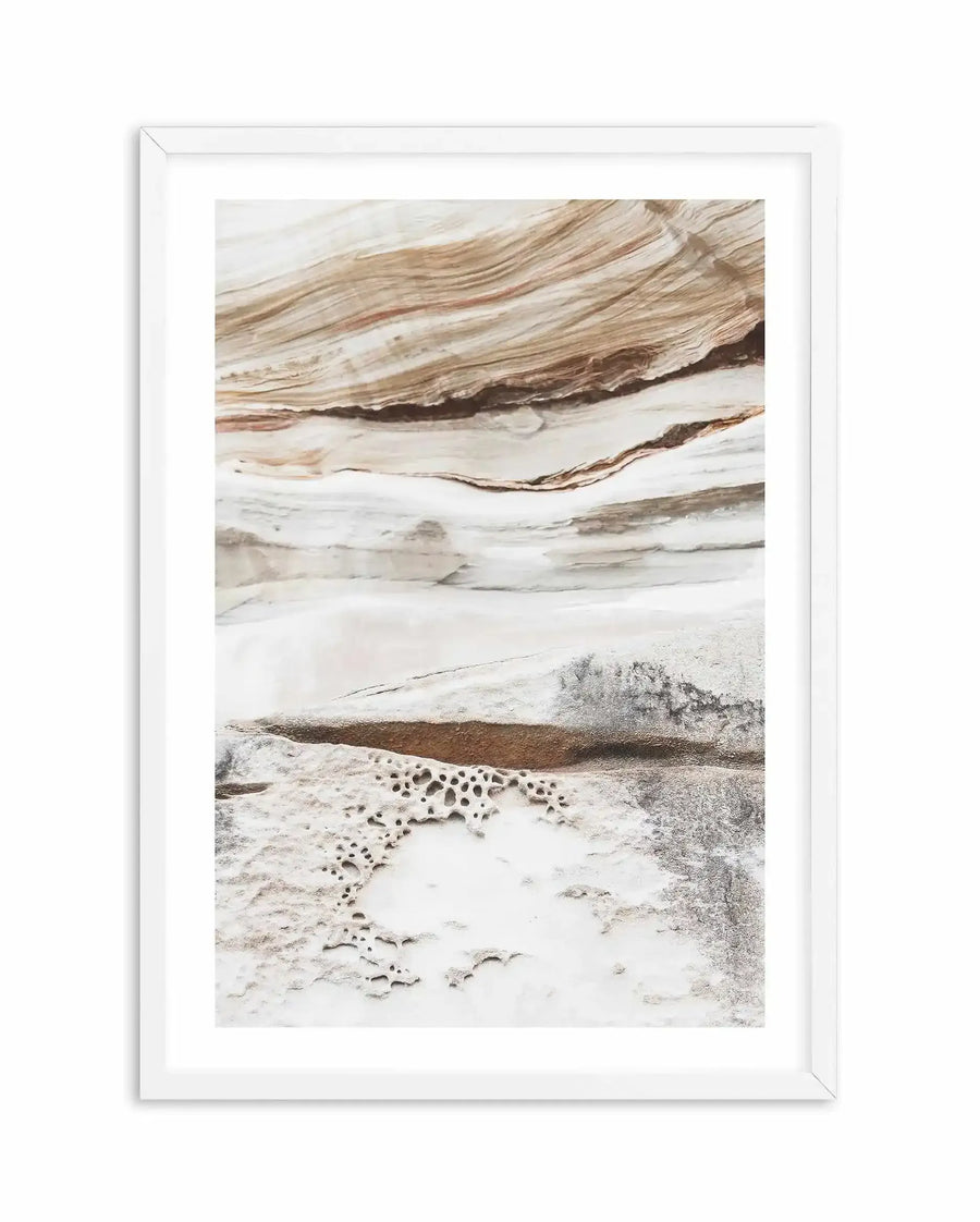 Framed art print featuring a close-up photograph of natural rock formations with horizontal layers of warm brown, cream, and white, with a white frame and white border. The lower section of the image shows textured rock with small, irregular holes.