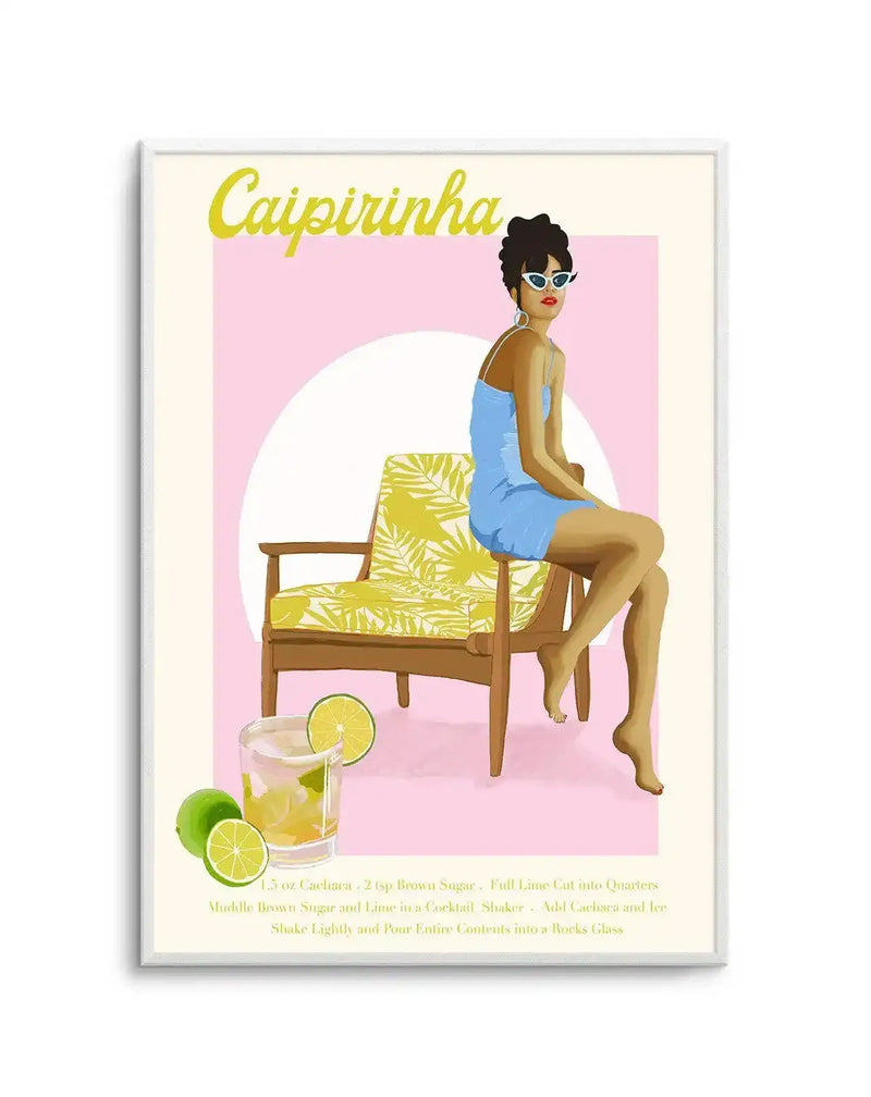 "Illustration art print featuring a woman in a light blue dress and white sunglasses sitting on a yellow patterned chair, with a glass of Caipirinha and limes in the foreground, set against a soft pink and white background, displayed in a white frame with a white border."