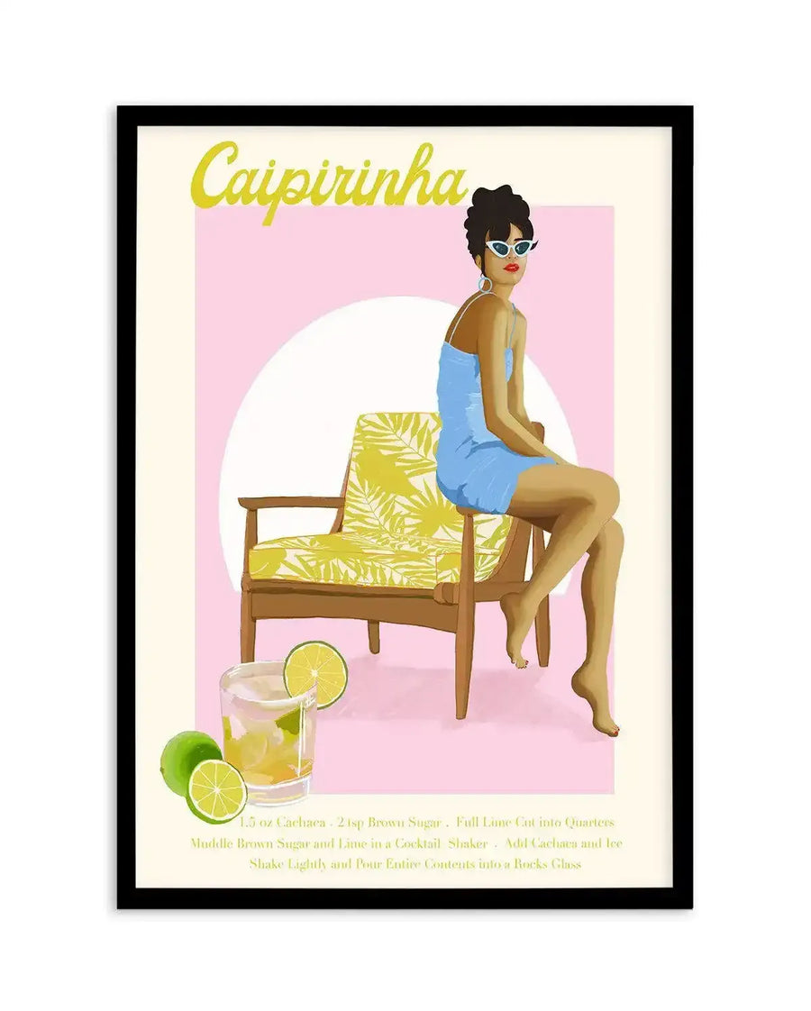 Caipirinha cocktail recipe art print by Jenny Liz Rome, featuring an illustration of a woman with dark hair and sunglasses wearing a blue dress, seated on a mid-century wooden chair with yellow palm leaf patterned upholstery against a soft pink background. A glass of caipirinha with lime slices sits in the foreground. Yellow script text reads "Caipirinha" at top with recipe instructions in yellow text at bottom. The artwork is framed in a black frame with white border.