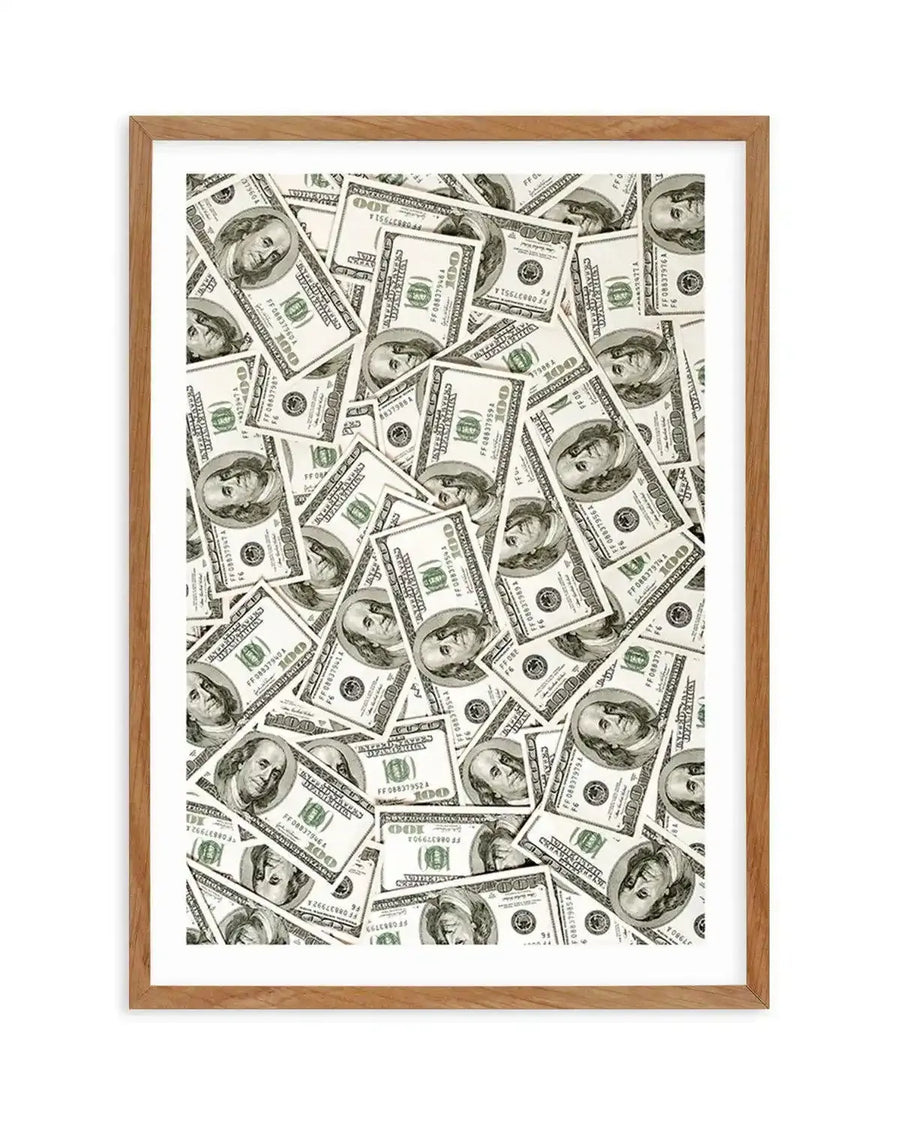 Framed art print featuring a dense, chaotic pile of one hundred dollar bills, with Benjamin Franklin's portrait visible on many of the scattered notes, displayed in a natural oak frame with white border. The composition creates a sense of abundance and wealth.