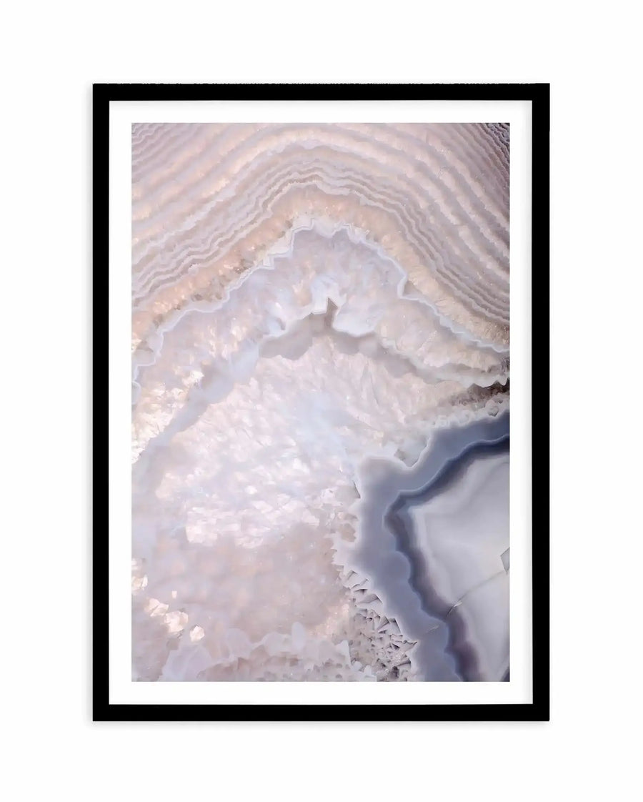 Abstract art print featuring layered, concentric curved lines in soft taupe, lavender, and cream tones resembling a cross-section of agate or geode. The composition shows delicate striations radiating outward with textured, crystalline formations in the center. Mounted in a black frame with white border. The overall effect is organic and geological with a serene, minimalist aesthetic.