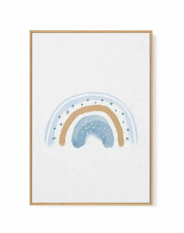 Framed canvas art print featuring a watercolor-style illustration of a dreamy rainbow with layered arcs in soft blue, tan, and white. The innermost arc is mist blue with white dots resembling falling snow or stars. The middle arc is warm tan or gold. The outer arc is pale blue decorated with small dark blue star symbols scattered around the curve. The artwork is centered on a white background and displayed in a natural wood frame with a white border.