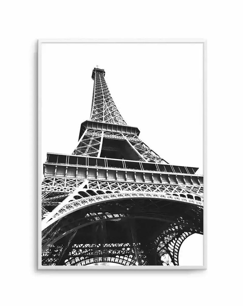 Black and white photograph of the Eiffel Tower shot from a low angle, capturing the intricate iron lattice structure and architectural details. The composition emphasizes the tower's geometric framework, arches, and multiple levels against a white background. The high-contrast monochrome image showcases fine details of the metal ironwork and construction. The art print is displayed in a silver-toned frame with a white border.