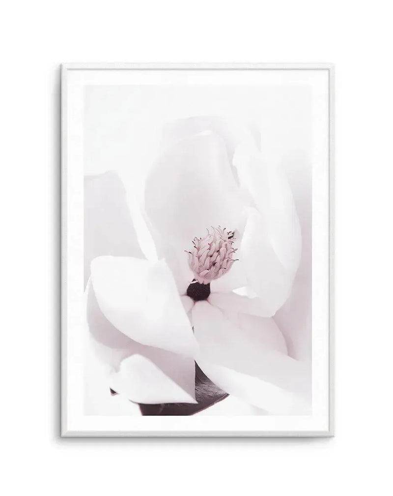 Framed art print featuring a close-up photograph of a white magnolia flower with delicate petals unfurling around a pale pink stamen with dark center. The image has a soft, minimalist aesthetic with a predominantly white and cream color palette and subtle blush pink tones. The photograph is mounted in a silver-toned frame with a white border, displayed against a white background.