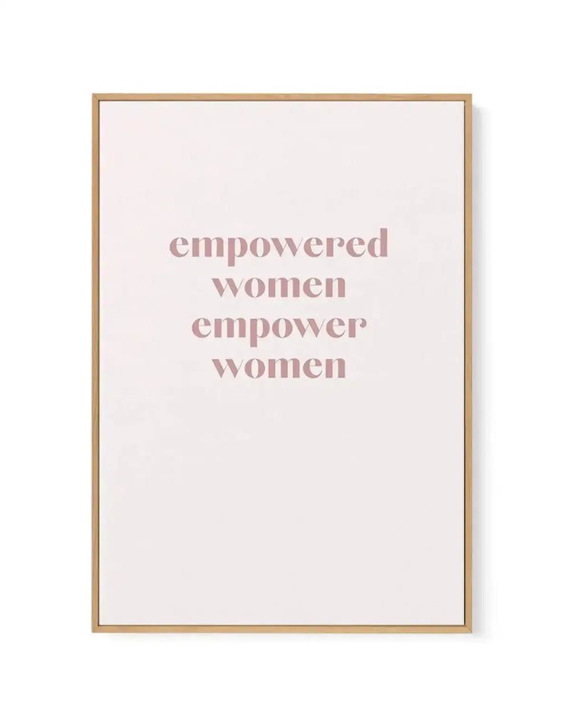 Framed canvas art print with a natural wood frame displaying centered text in dusty rose serif font on a cream background. The text reads "empowered women empower women" in four stacked lines. The canvas has a white border between the artwork and wooden frame.