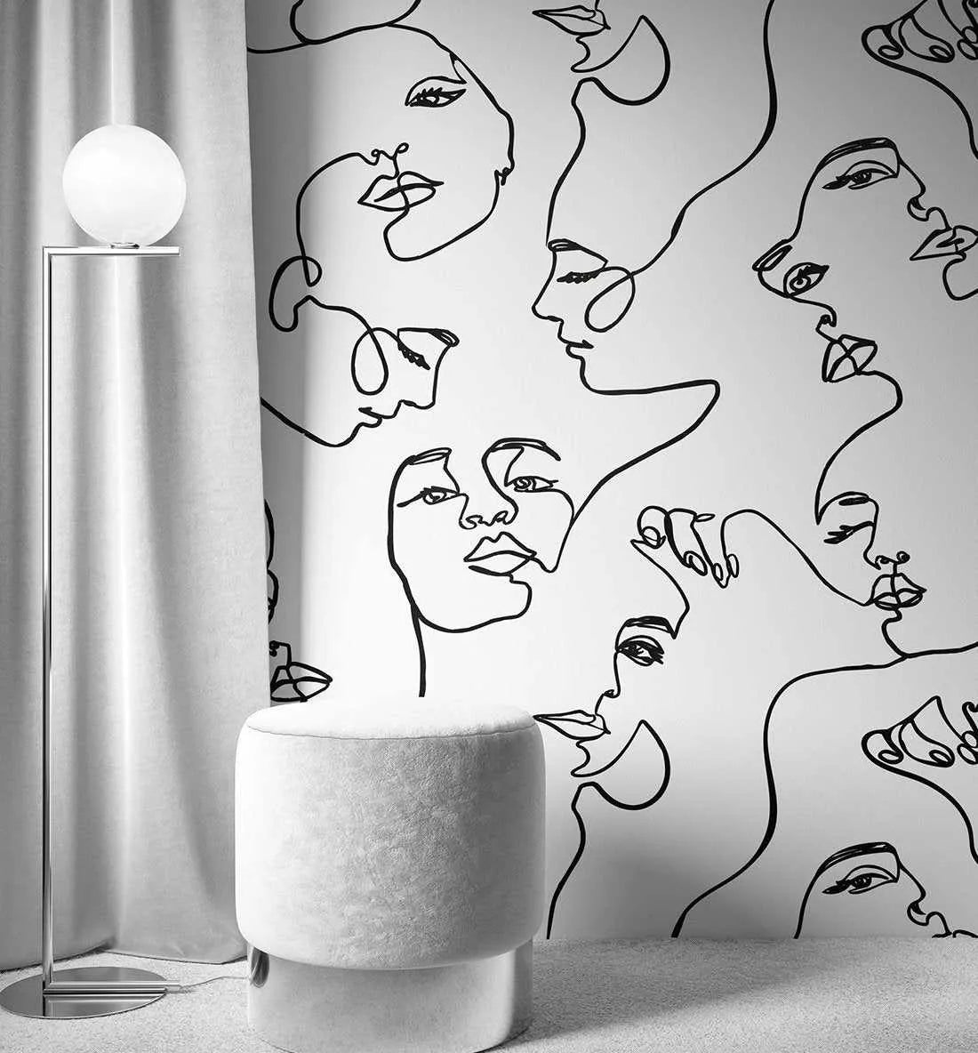 Peel and stick wallpaper featuring a repeating pattern of abstract line art faces in black on a white background, displayed on a wall in a minimalist living room. The design depicts various female faces in profile and frontal views, created with continuous, flowing lines. The room includes a tall, modern floor lamp with a spherical white shade and a round, light grey velvet ottoman.