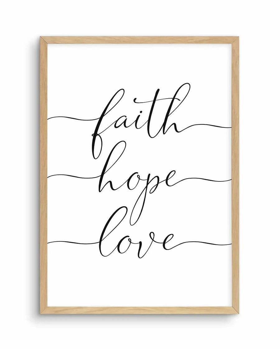 Framed art print with natural wood border displaying three words in elegant black cursive script stacked vertically on a white background: "faith" at the top, "hope" in the middle, and "love" at the bottom. Thin horizontal lines extend from each word across the width of the design. The minimalist composition features delicate, flowing handwritten-style lettering against a clean white background.